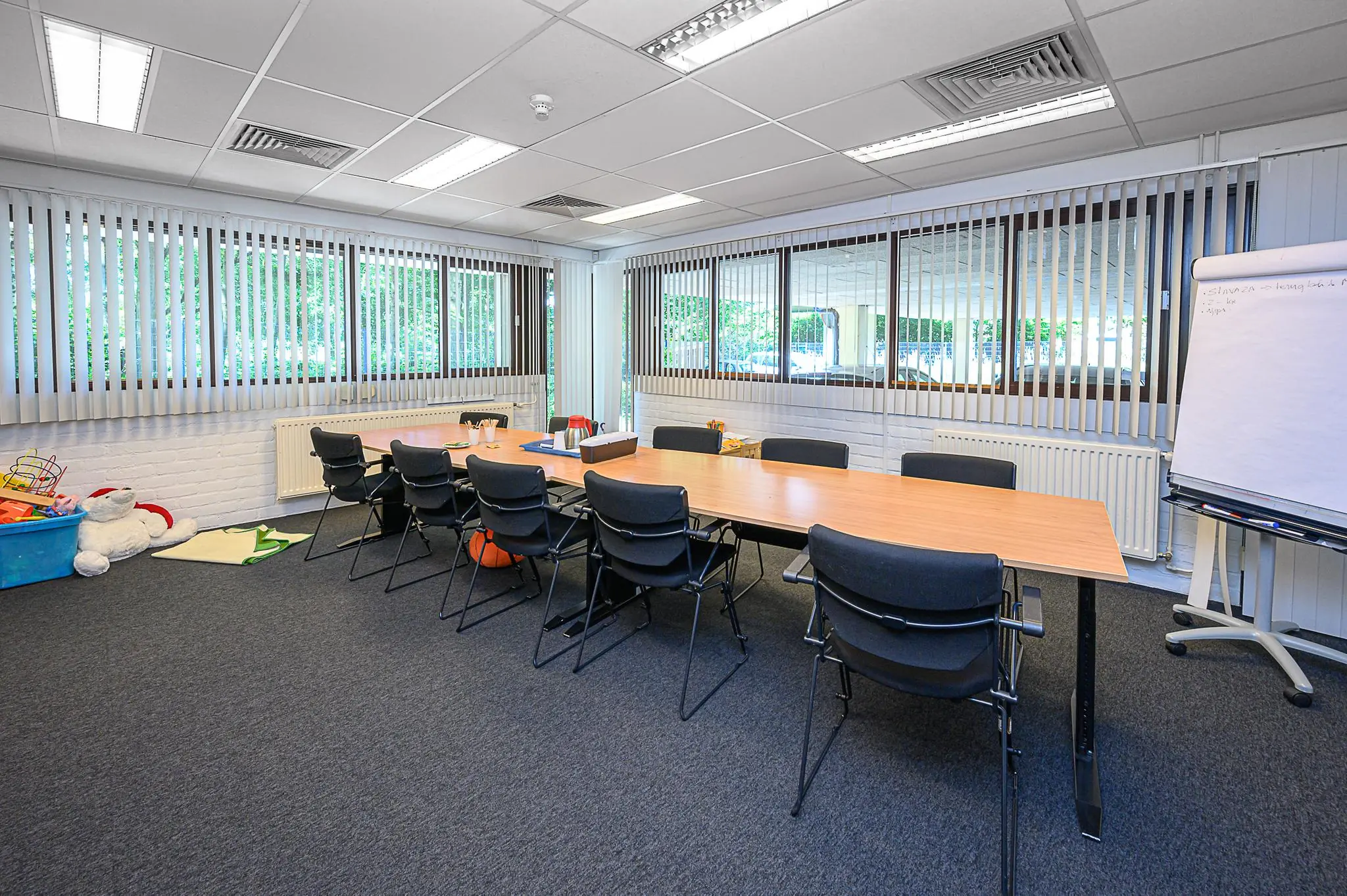 Vergaderruimte De Linie met een lange tafel, meerdere stoelen, flip-over en kinderspeelgoed in de hoek.